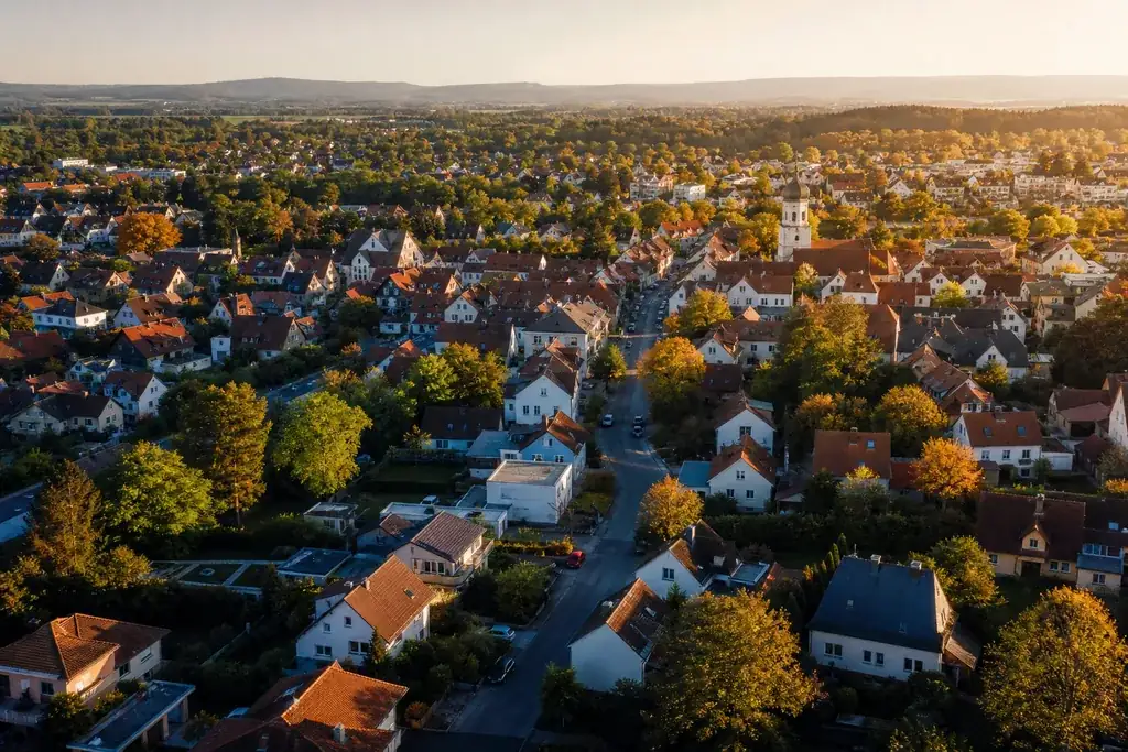 Luftaufnahme einer typischen deutschen Wohnstadt mit roten Ziegeldächern und viel Grün an einem sonnigen Tag.