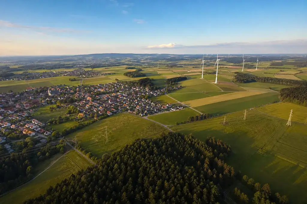 Luftaufnahme einer vielfältigen deutschen Landschaft mit Ortschaften, Feldern, Windrädern und Stromleitungen, Sinnbild für Strompreise über viele Regionen hinweg.