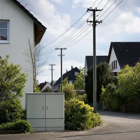 Illustration zum Abschnitt „Netzgebiet ist nicht gleich Stadtgebiet“ im Ratgeber „Grundversorger finden über die Postleitzahl“: ein Wohnviertel mit Stromleitungen und einem Verteilerkasten.